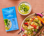 An overhead image of a package of Greek Tzatziki Dip Spice & Easy next to a finished bowl of the dip and a plate of chicken skewers.