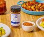 An image of a jar of homestead seasoning next to a bowl of the seasoning as well as a breakfast spread of potatoes, eggs, bacon, fruit, and coffee. 