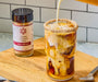 Image of a salted caramel spice rimmed latte with milk being poured in, next to a jar of salted caramel spice.